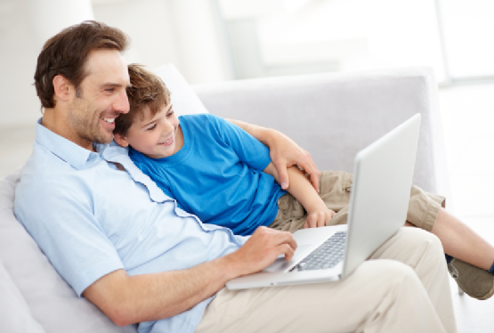 Father and son sitting together on sofa using laptop