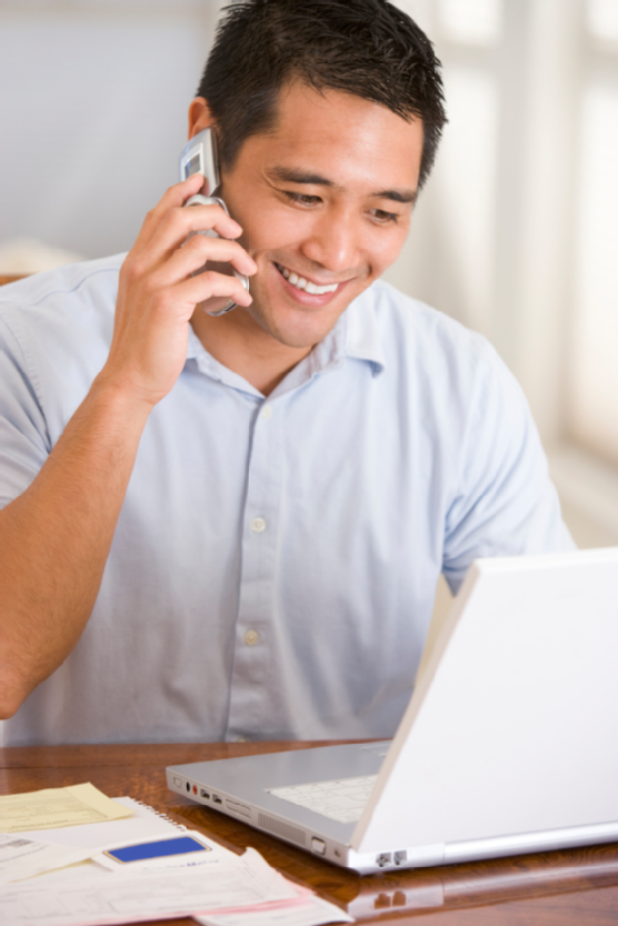 Man at home on mobile phone using laptop smiling